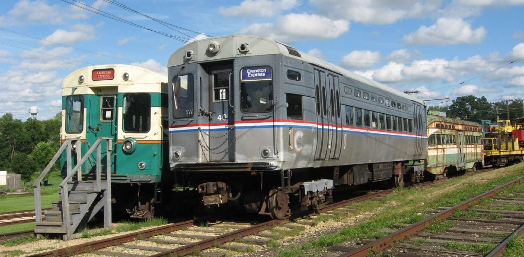 A group of old trolleys outdoors on tracks at the Fox River Trolley Museum