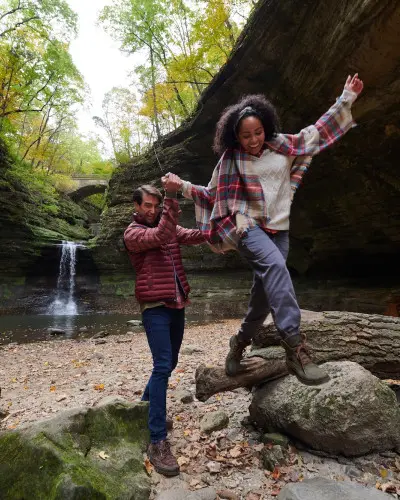 Two people climbing on rocks in front of a rock waterfall