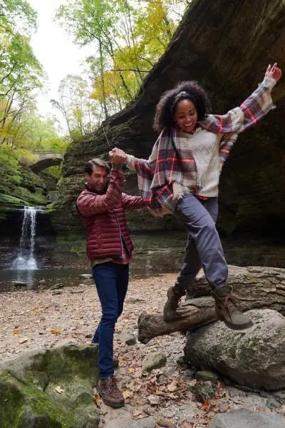 Two people climbing on rocks in front of a rock waterfall